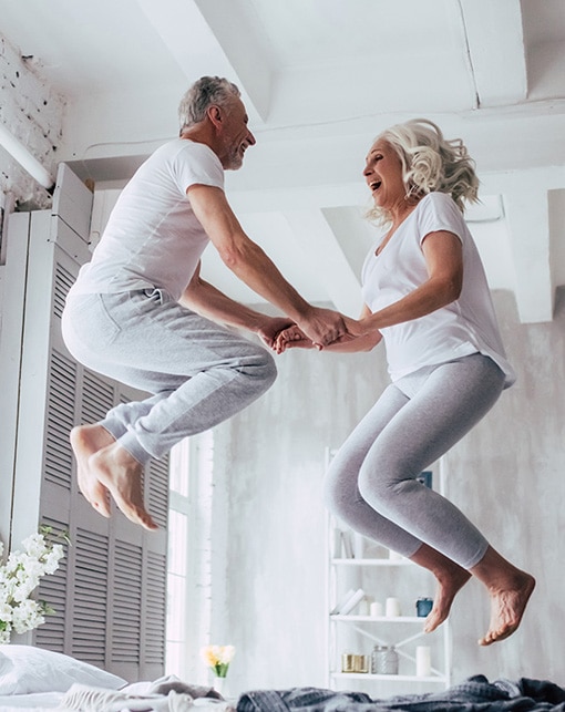 Couple de seniors heureux sautant sur un lit